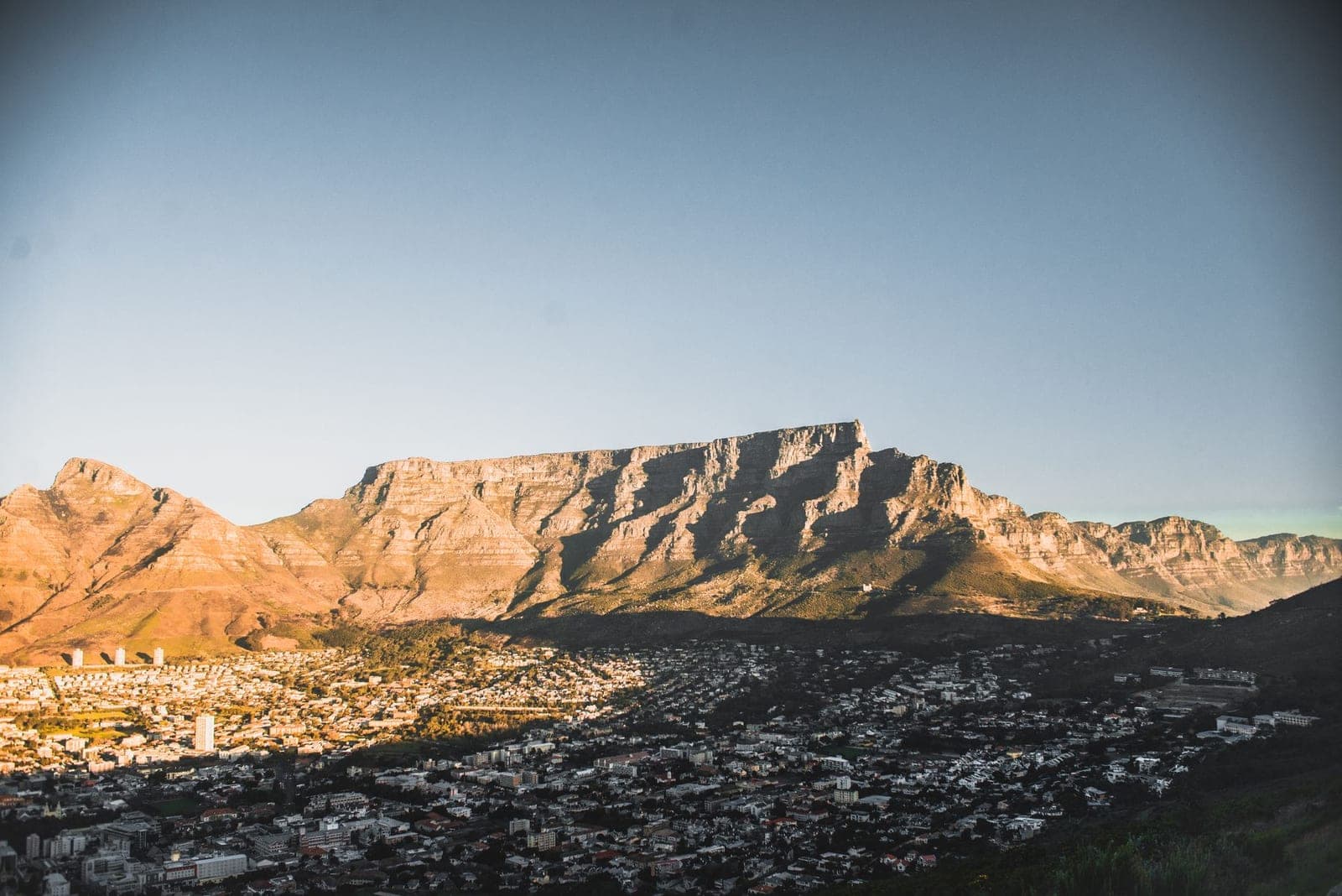 Cape Town spread below Table Mountain at sunset, the city lights coming on beneath the ridge.