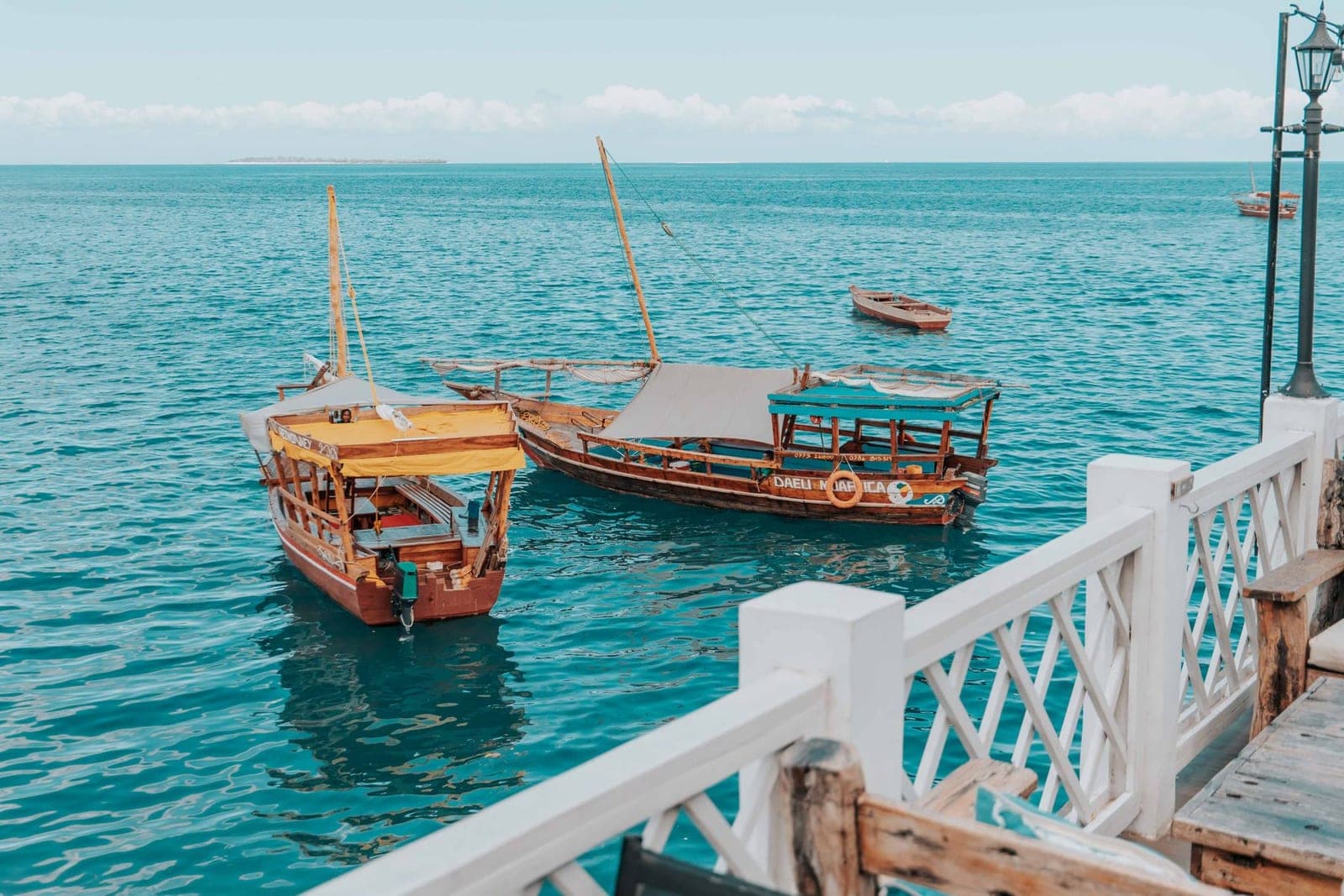 Traditional dhows moored on turquoise water off Zanzibar, seen from a wooden jetty.
