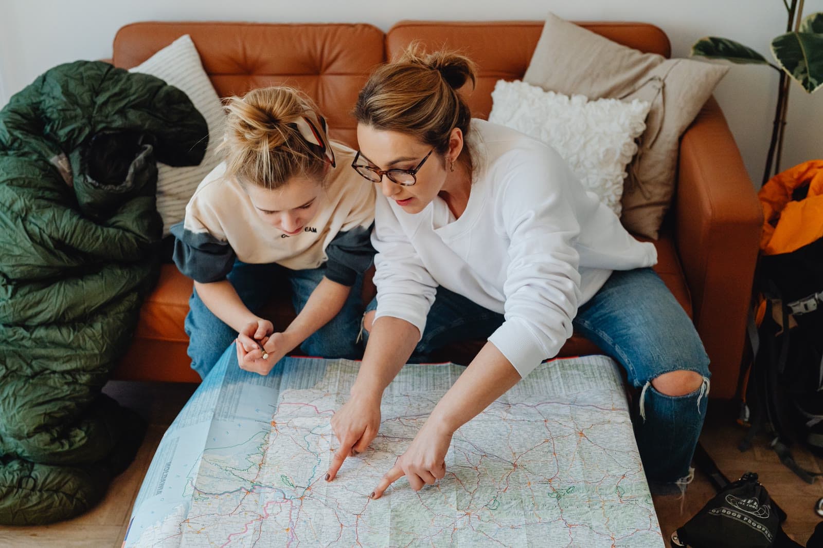 A mother and daughter planning a route together over a paper map, hiking gear beside them.