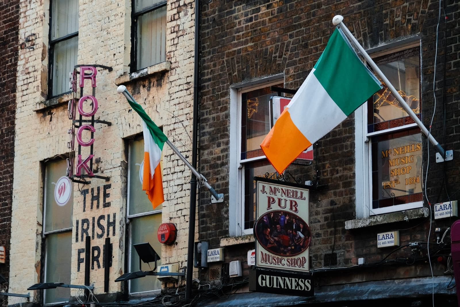 The facade of J. McNeill's pub in Dublin, tricolours flying above signs for its music shop and Guinness.