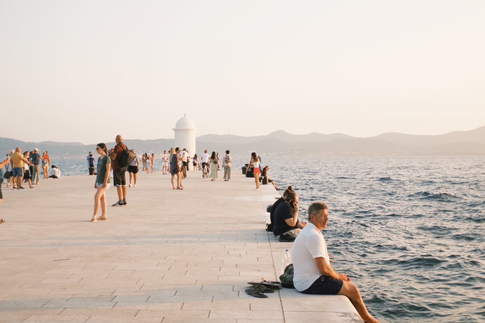 People gathered along a stone waterfront in the evening light.