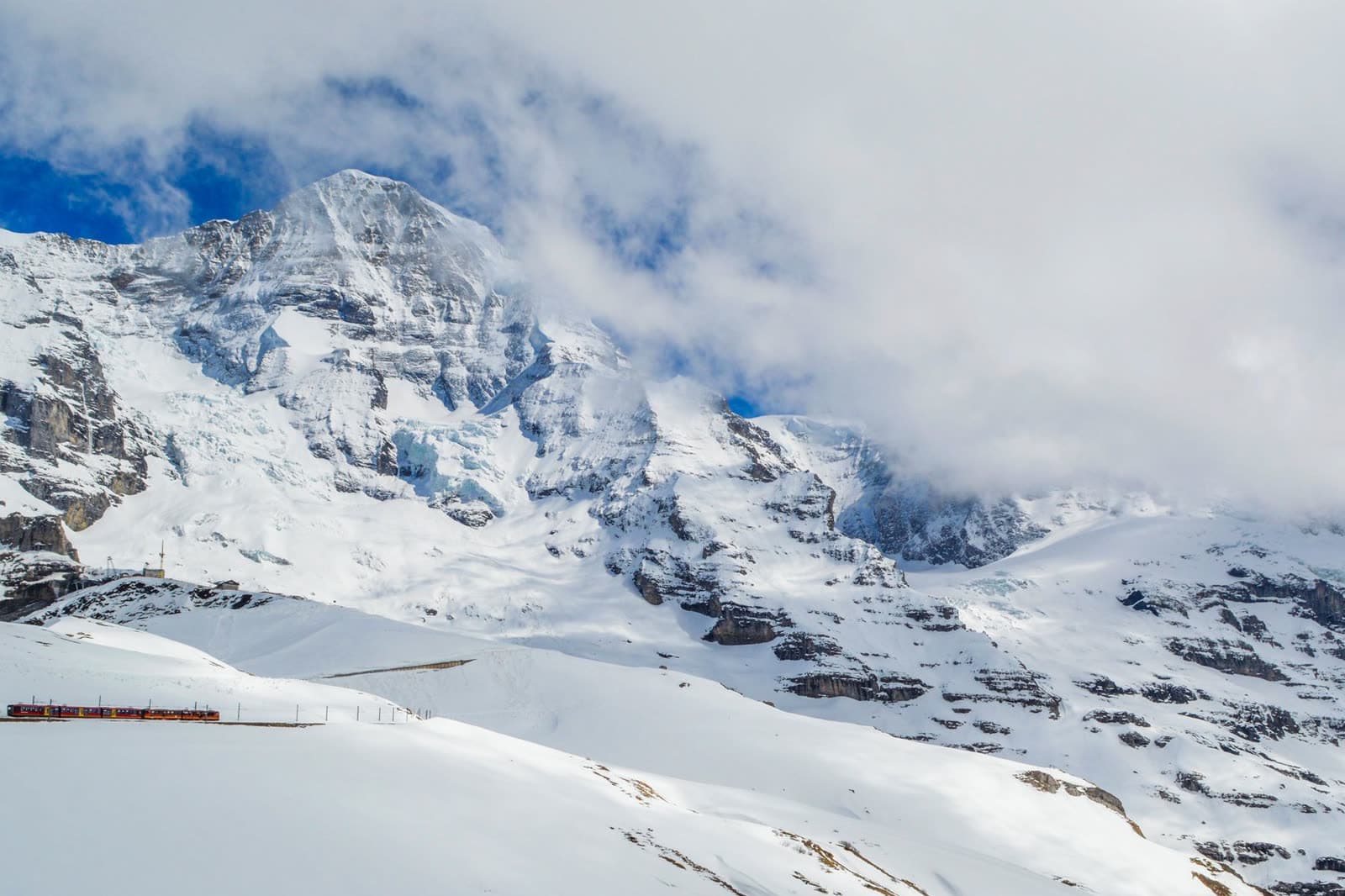 A red alpine train crossing a high valley below snow-covered peaks.
