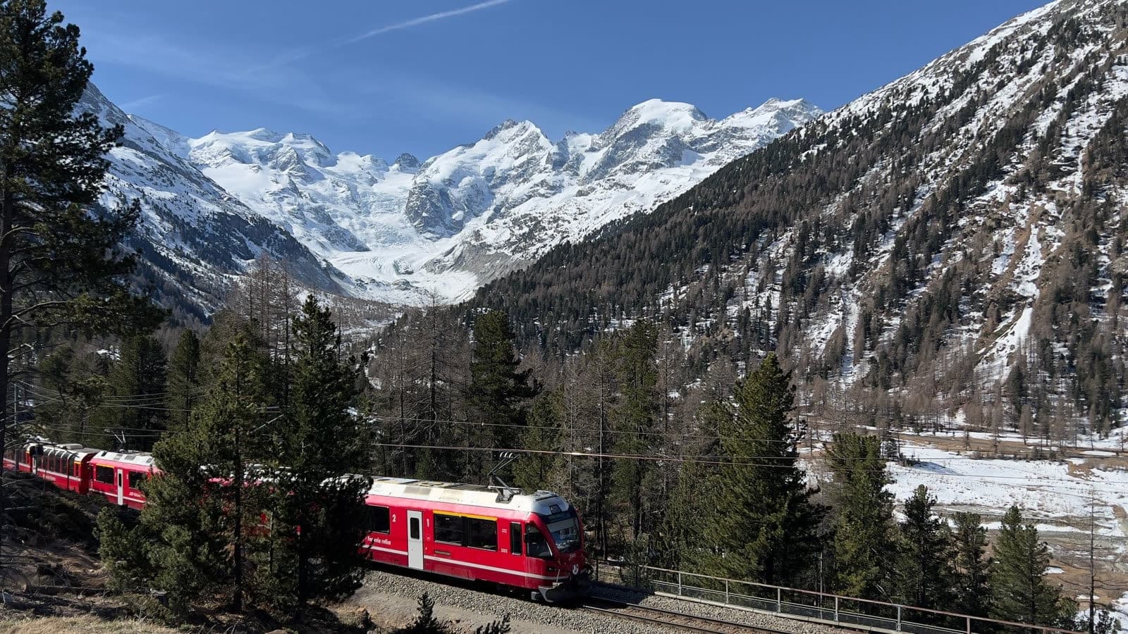Red mountain train running through a snowy Alpine valley