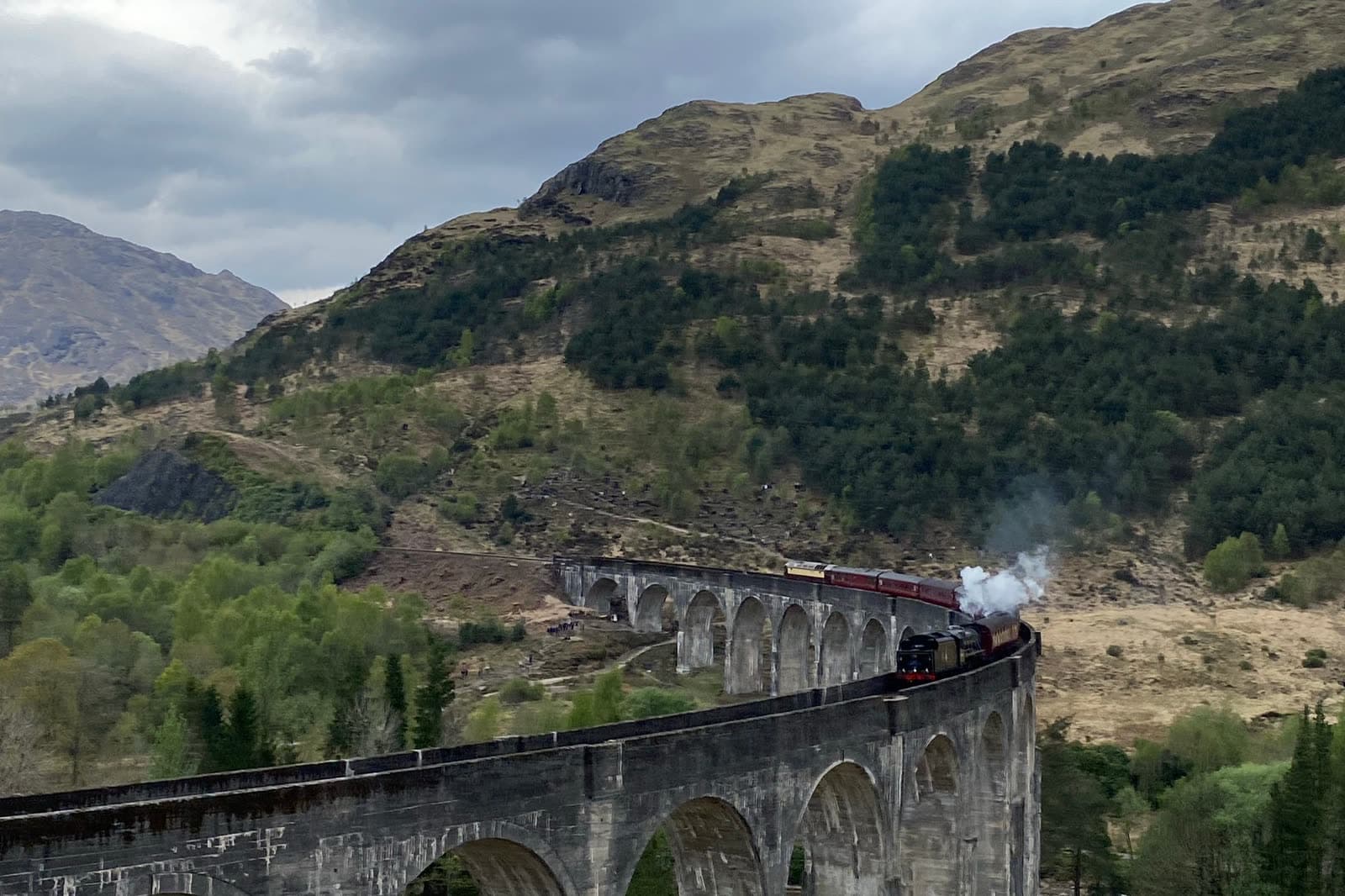 A steam train crossing the curved arches of the Glenfinnan Viaduct.