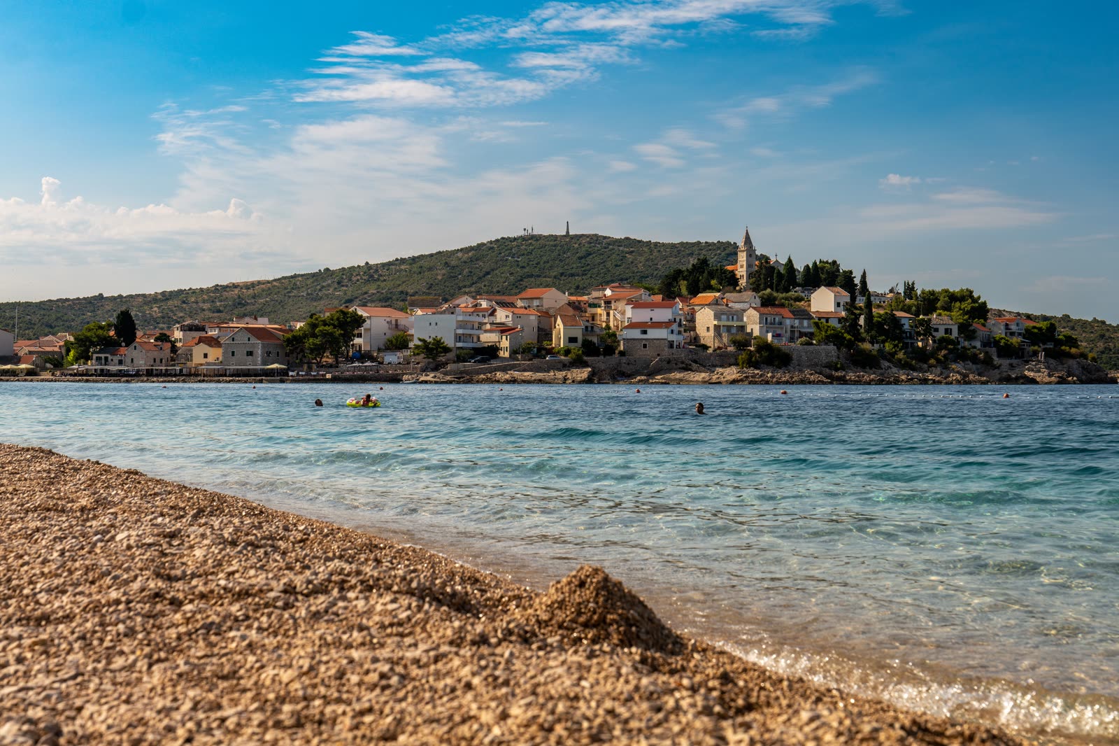 A coastal town above a pebble beach and clear summer water.