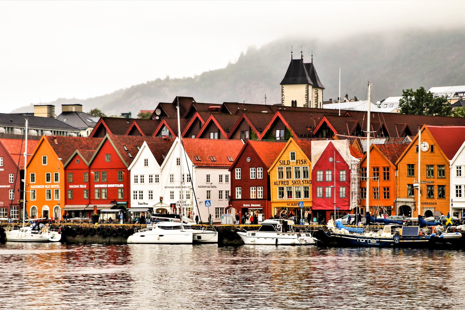 The coloured timber warehouses of Bryggen along the Bergen waterfront, boats moored in front.
