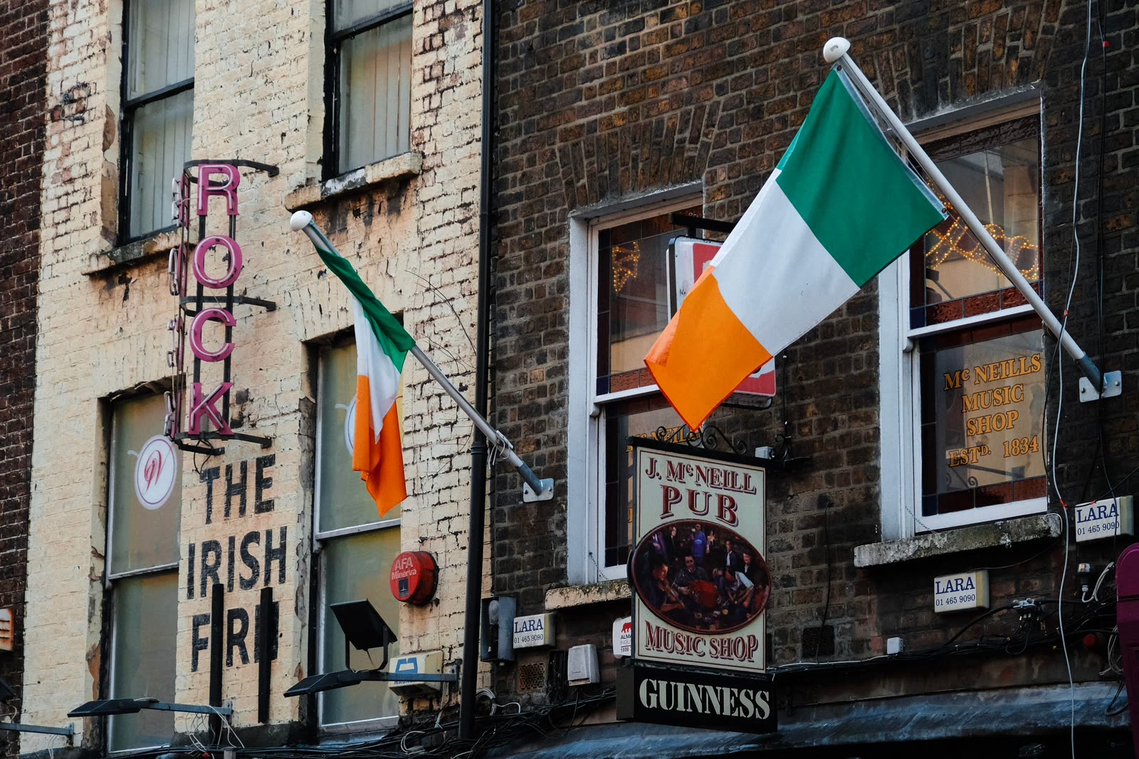 The facade of J. McNeill's pub in Dublin, tricolours flying above signs for its music shop and Guinness.