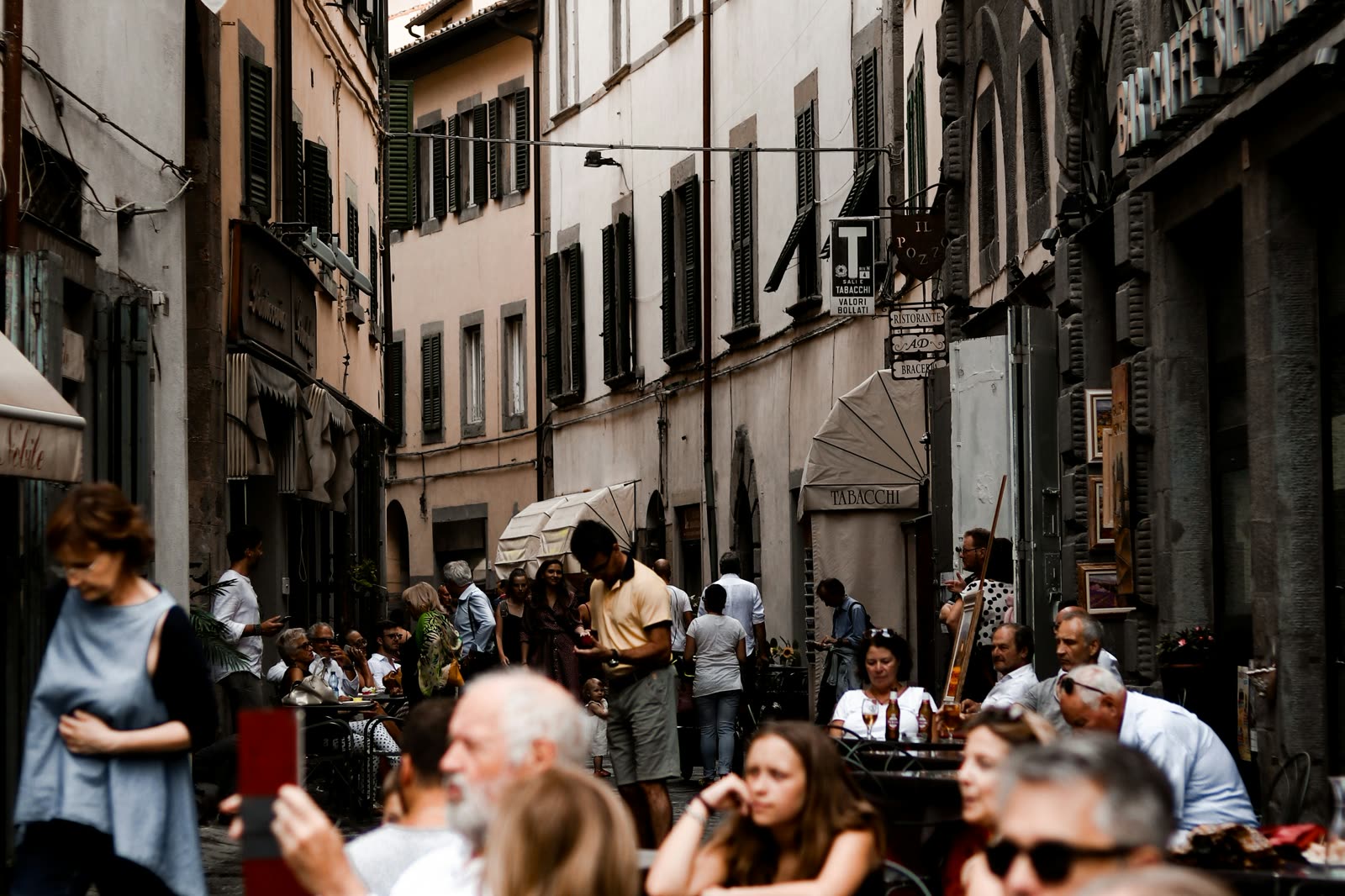 A narrow Roman street crowded with café tables and evening walkers.