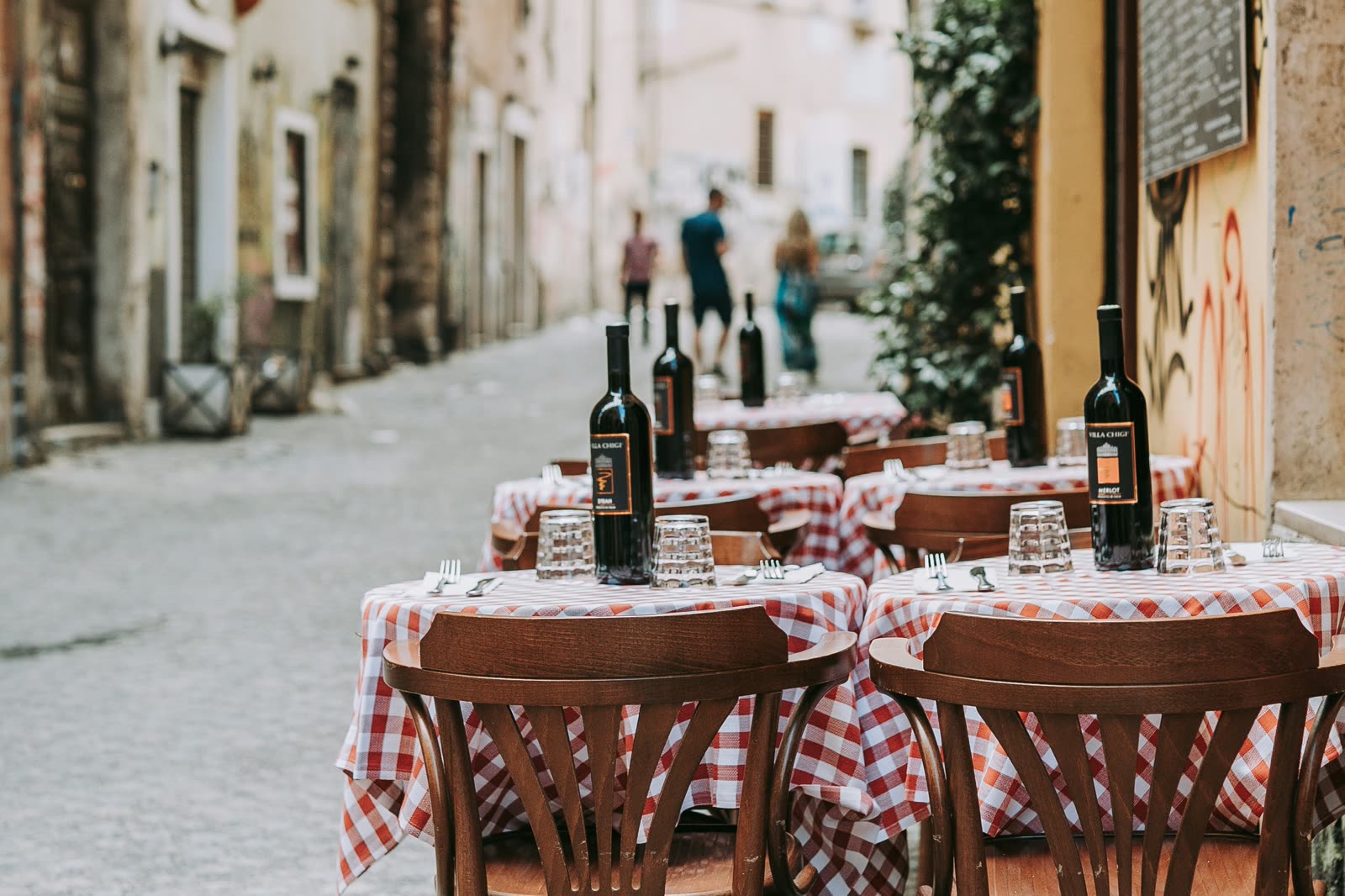 Trattoria tables set with checked cloths and bottles of red wine.