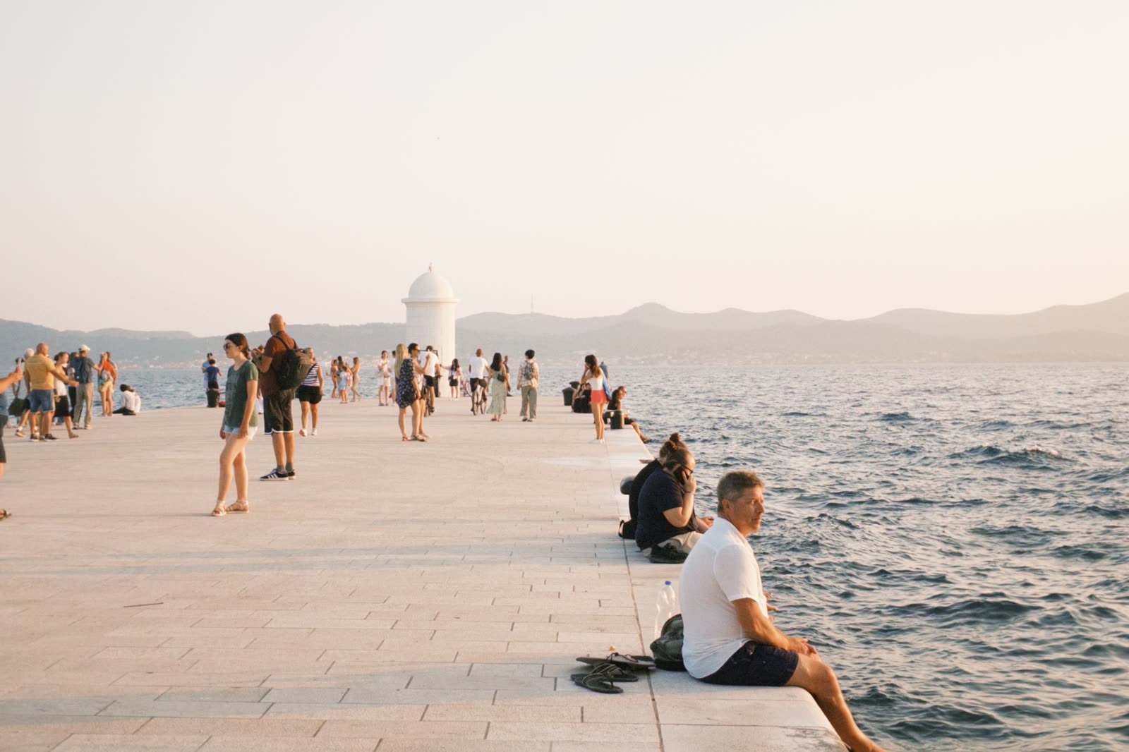 People gathered along a stone waterfront in the evening light.