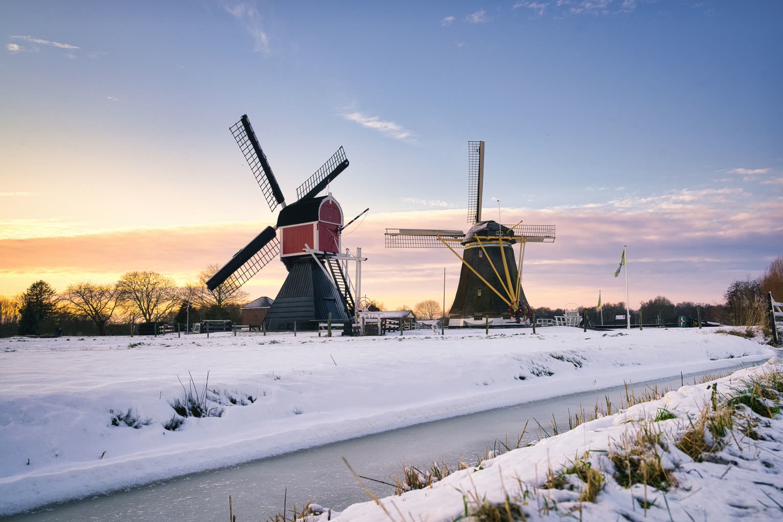 Two windmills beside a frozen canal at sunrise, snow lying across the fields.