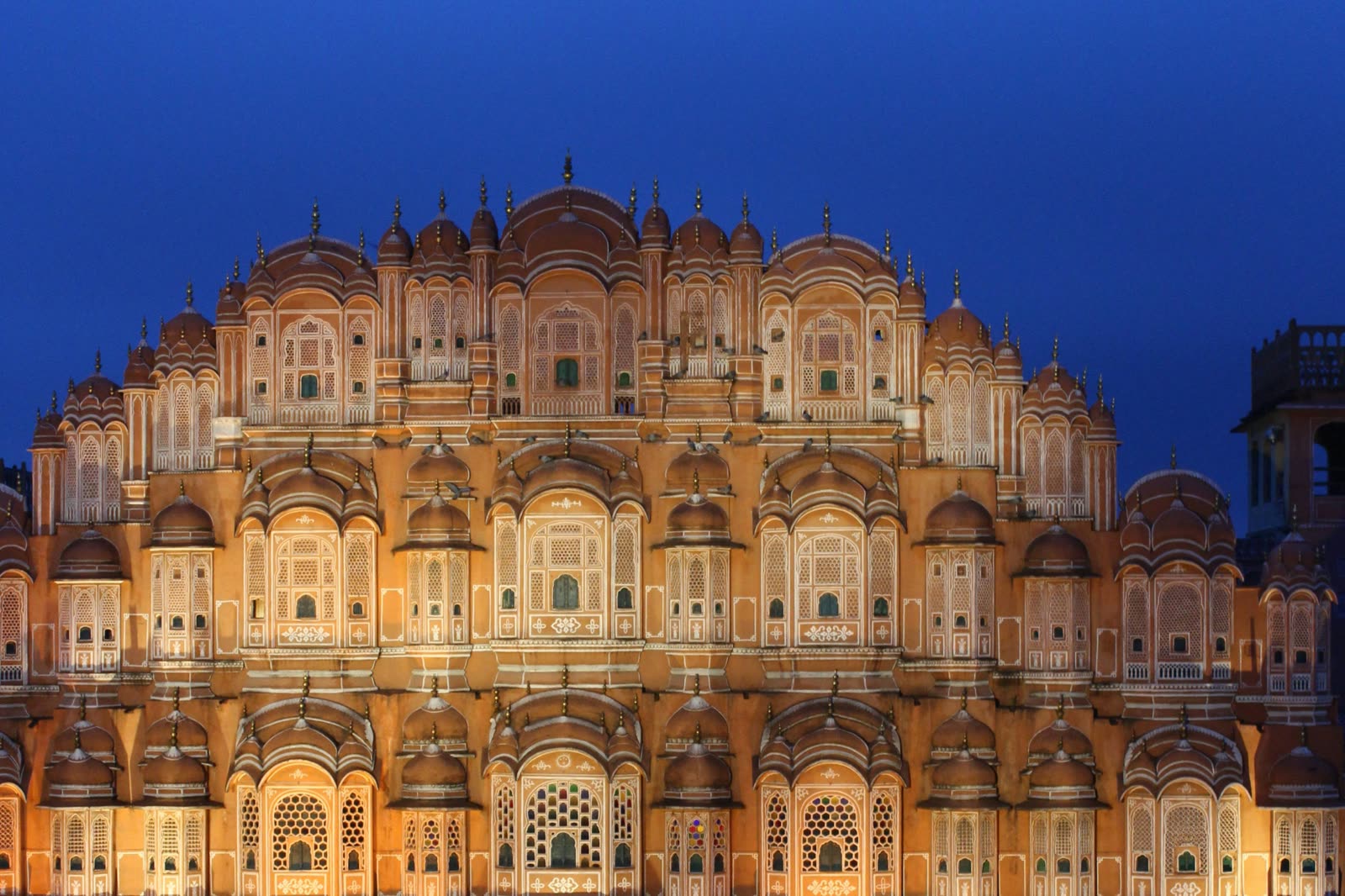 The Hawa Mahal in Jaipur, its honeycomb facade lit against a deep blue dusk sky.