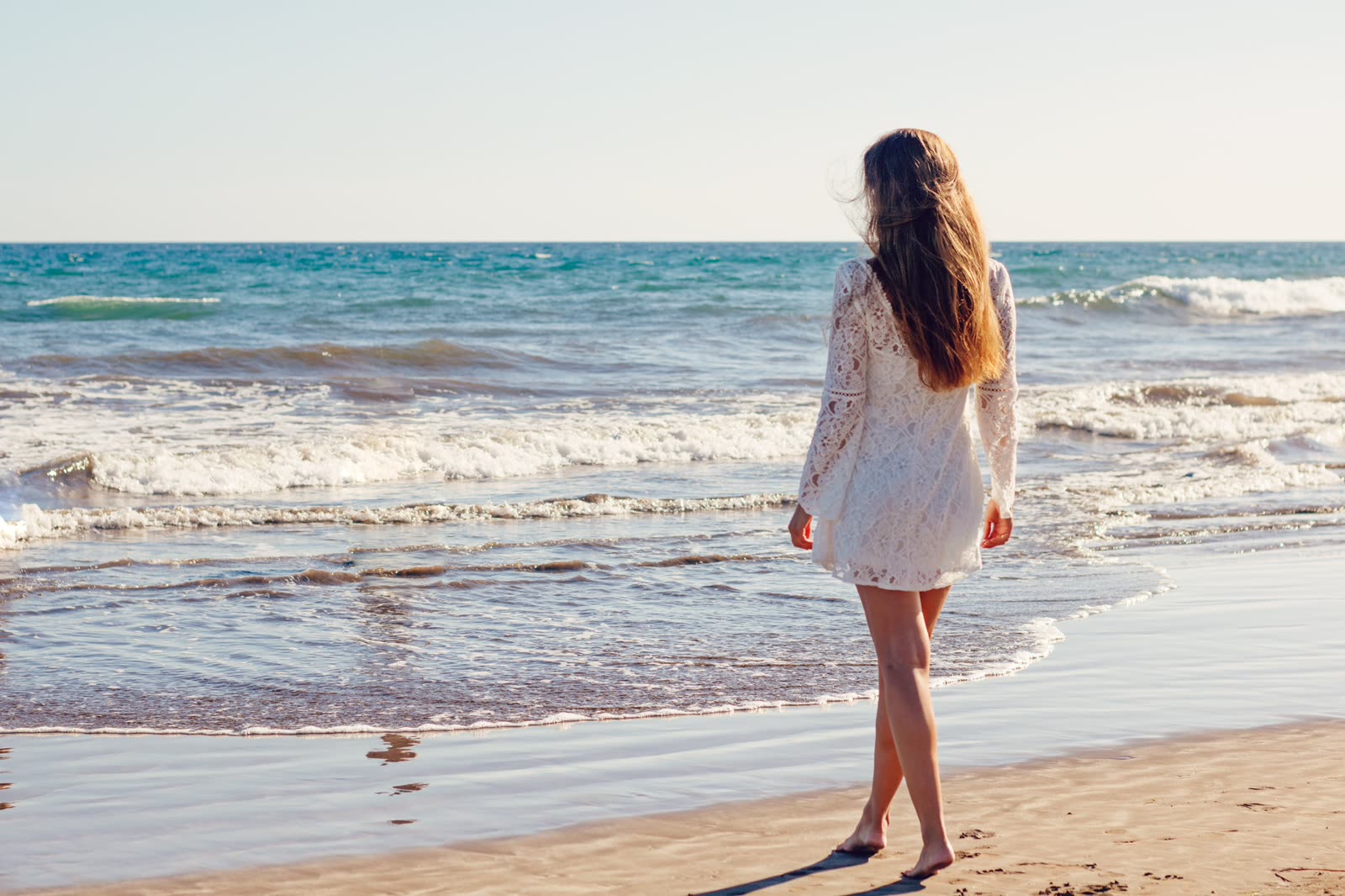 A woman walking the tideline of an empty beach.