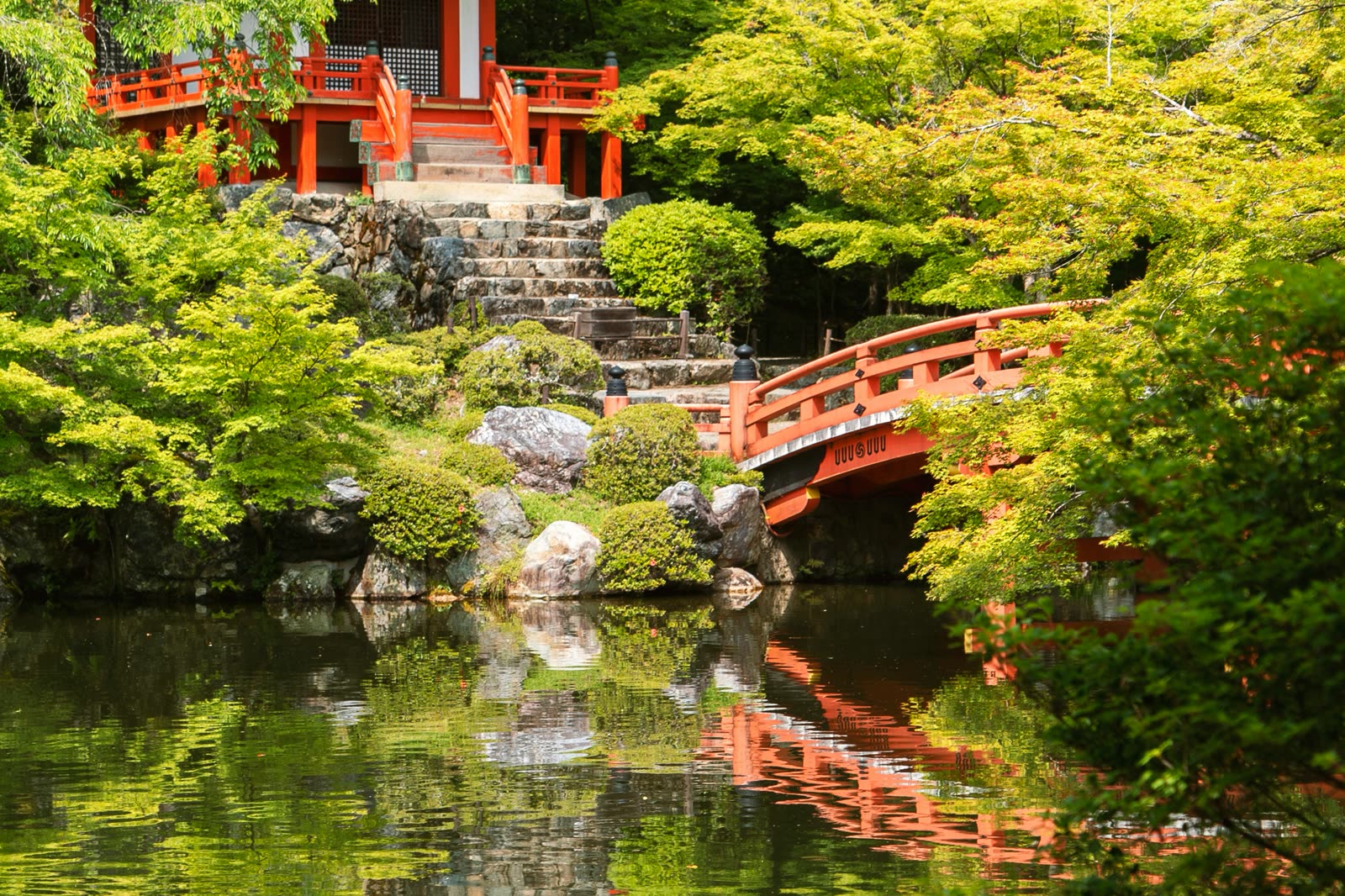 A vermilion bridge over a still pond in a Japanese landscape garden.