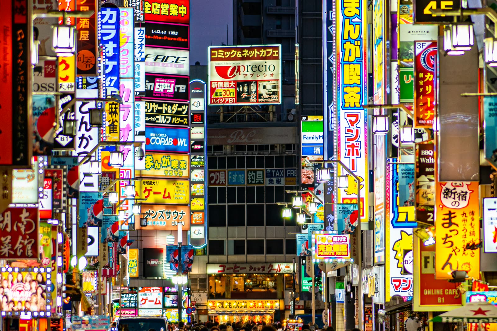 A Shinjuku street after dark, its buildings covered from street level to roofline in illuminated Japanese signage.