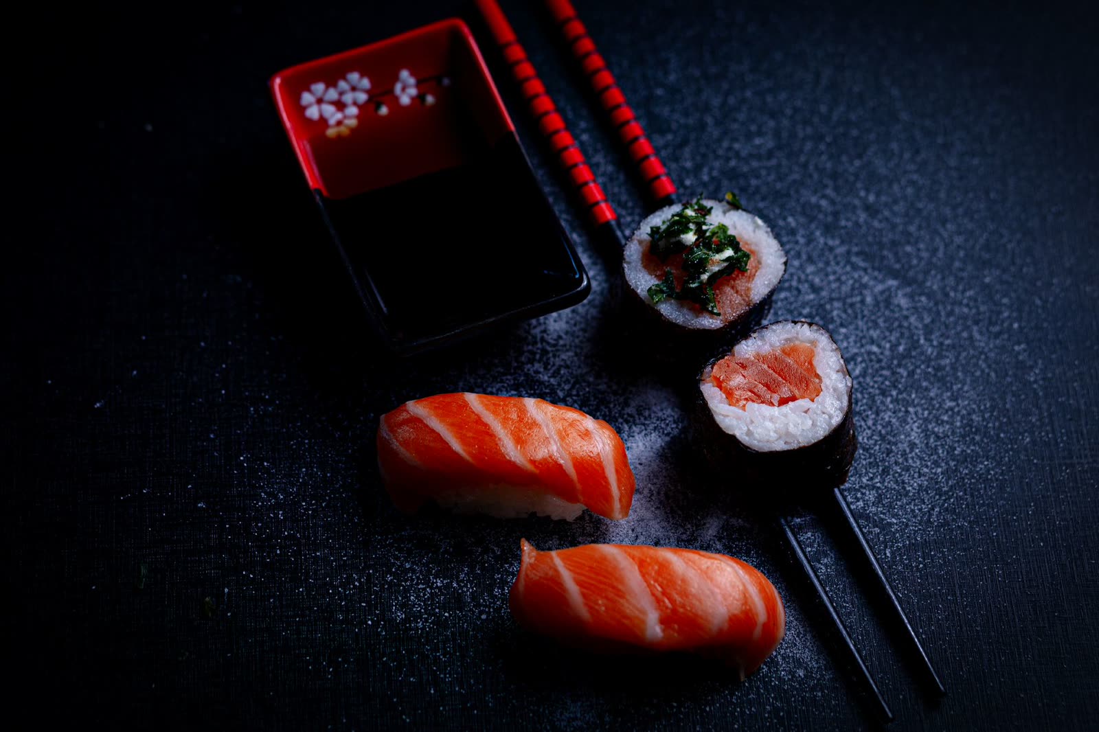 Nigiri and maki arranged on dark slate with soy and chopsticks.