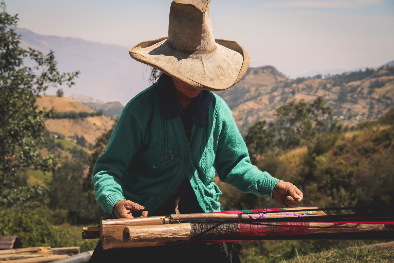 A weaver working a backstrap loom on a hillside in the Andes.