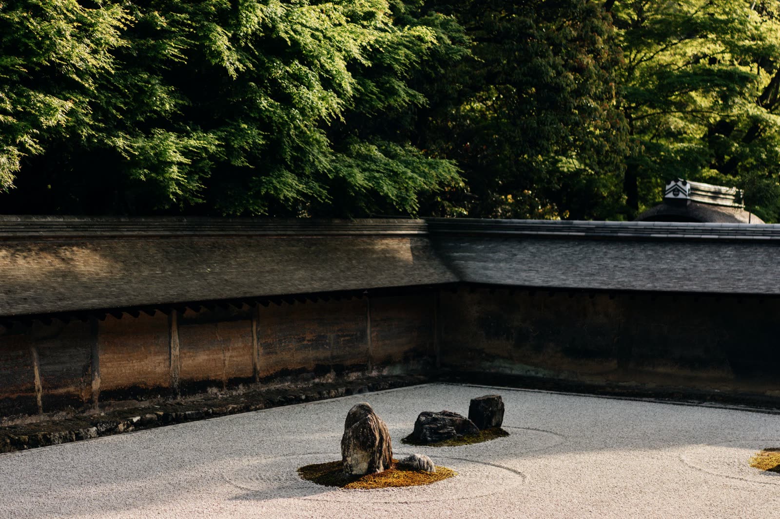A raked gravel Zen garden with moss-ringed stones, framed by clipped hedge.